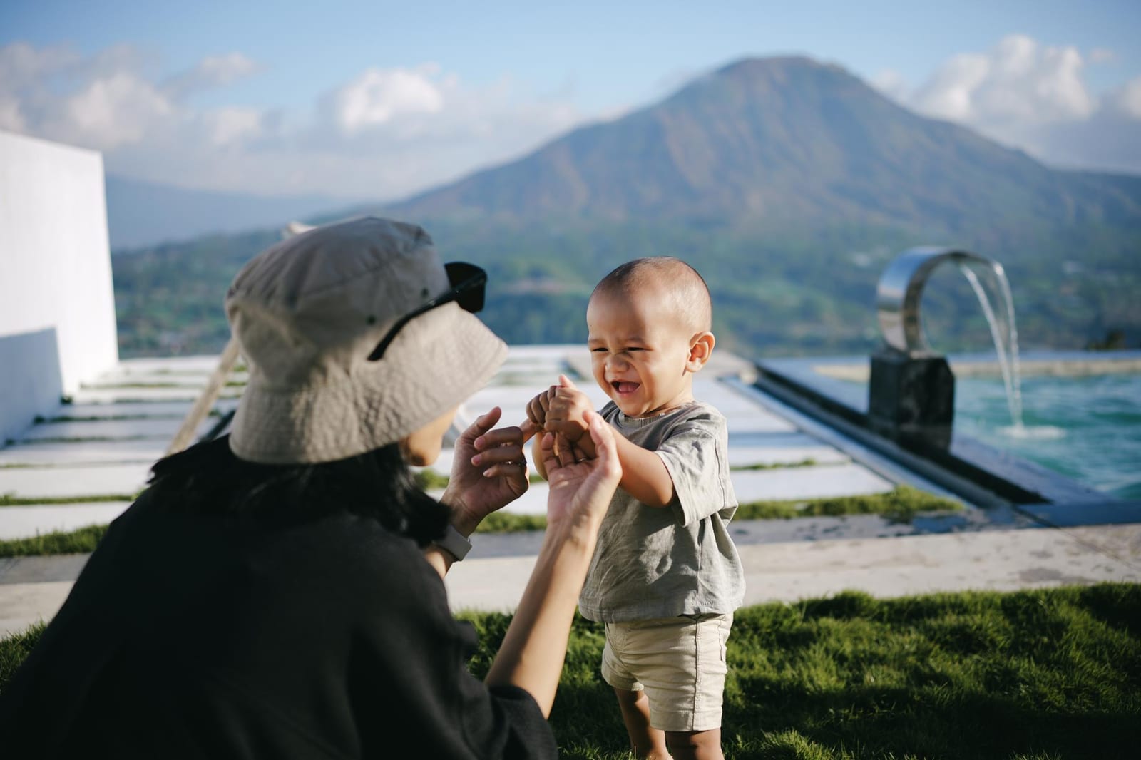 プールテラスの芝生で幼い子どもと遊ぶ母親、背景に山並みが見える様子